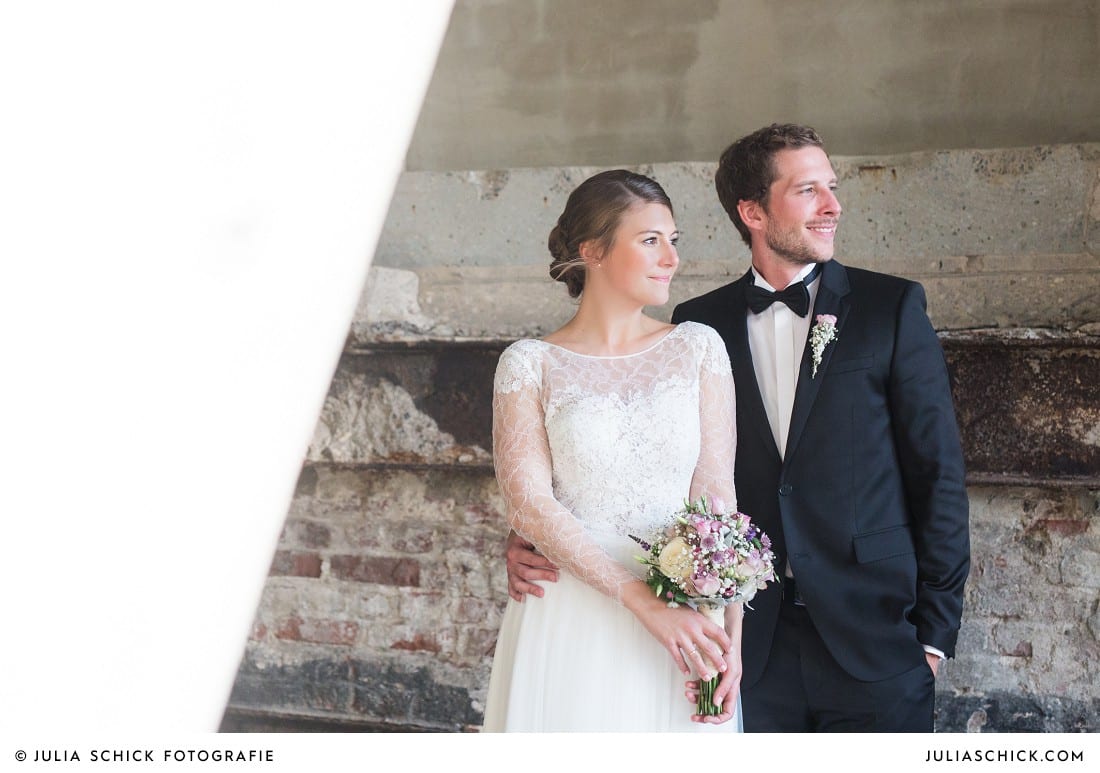 Brautpaar in Hochzeitskleid von Anna Kara und Smoking vor Ziegelwand mit Stahlträgern am Factory Hotel in Münster