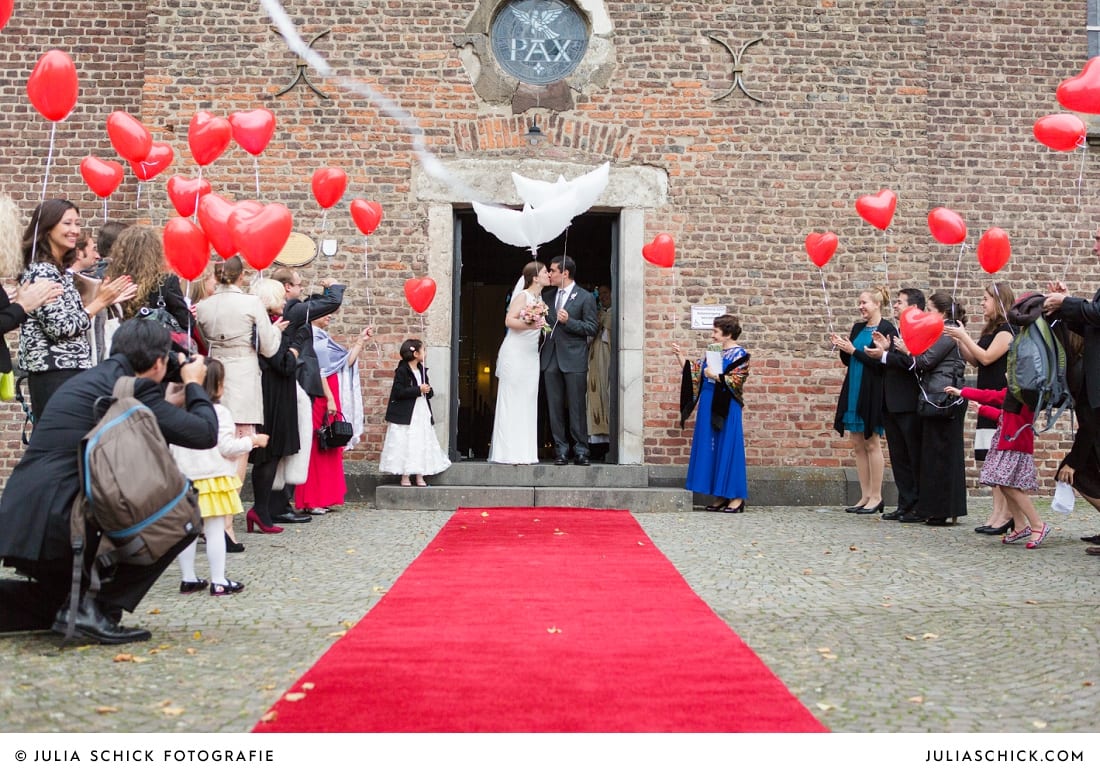 Brautpaar mit Luftballons steht im Portal der Sankt Antonius Kirche in Leverkusen Wiesdorf