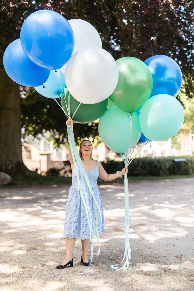 Trauzeugin mit großen Luftballons in grün, weiß und blau vor der Hochzeitslocation Haus Ruhr in Senden