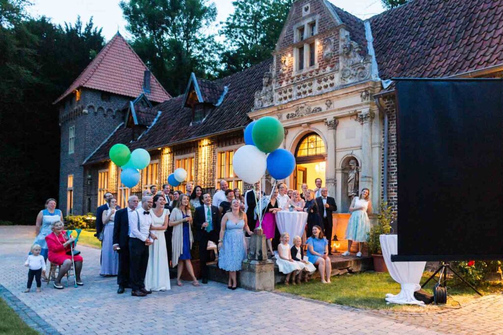 Hochzeitsgesellschaft schaut sich vor der Orangerie von Haus Ruhr eine Diashow an.