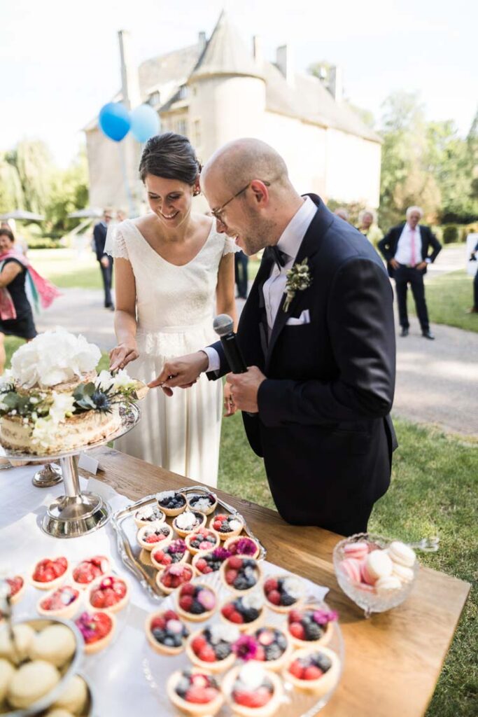 Hochzeitspaar schneidet Hochzeitstorte im Naked Cake Stil an im Vordergrund Törtchen und Macarons vor der Orangerie von Haus Ruhr