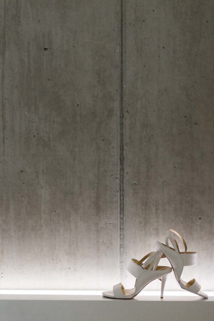 Brautschuhe in weiß vor betonwand in Suite des Factory Hotels in Münster