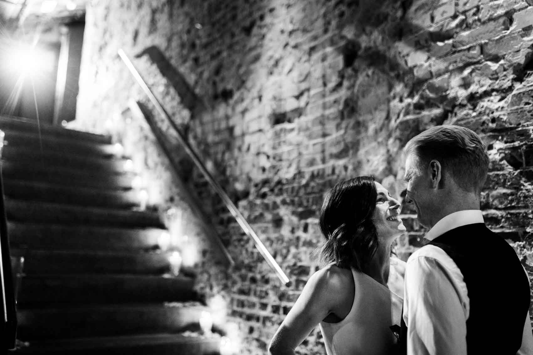 Braut und Bräutigam treffen sich am Ende der Treppe vr ihrer freien Trauung in der Hochzeitslocation Grey, die zum Factory Hotel gehört. Das Hochzeitsfoto ist in schwarz-weiß.