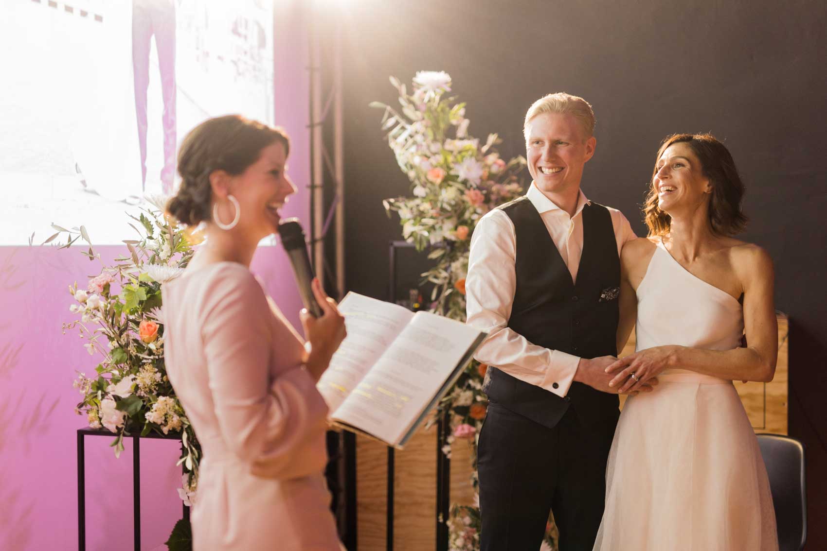 Lächelndes Brautpaar bei freier Trauung im Grey im Factory Hotel in Münster steht bei der Trauzeremonie gegenüber der Traurednerin Silvia Lobert.