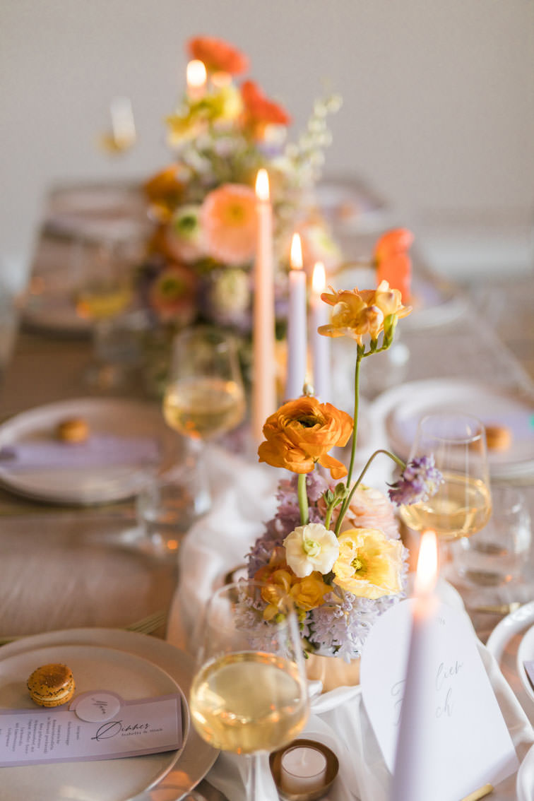 Gedeckter Hochzeitstisch mit Leinentischdecke und Ghostchairs im großen Saal der Kneisterei Münster. Blumendekoration in lila, orange und gelb