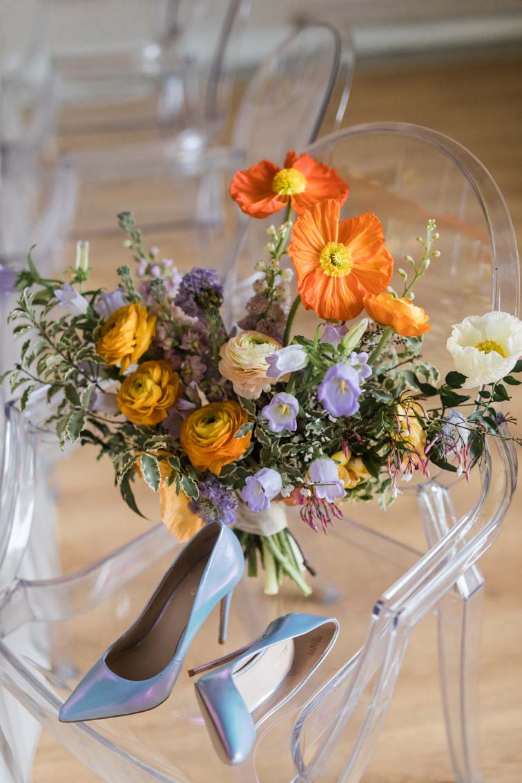 Brautstrauß in orange und violett und lila mit Klatschmohn und Ranungkeln und Glockenblumen auf einem Ghost Chair im Ballsaal der Kneisterei Münster