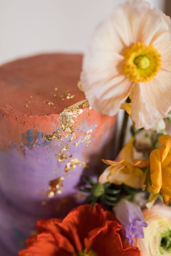 Detail einer Hochzeitstorte in orange und lila dekoriert mit Blattgold und Klatschmohn in orange