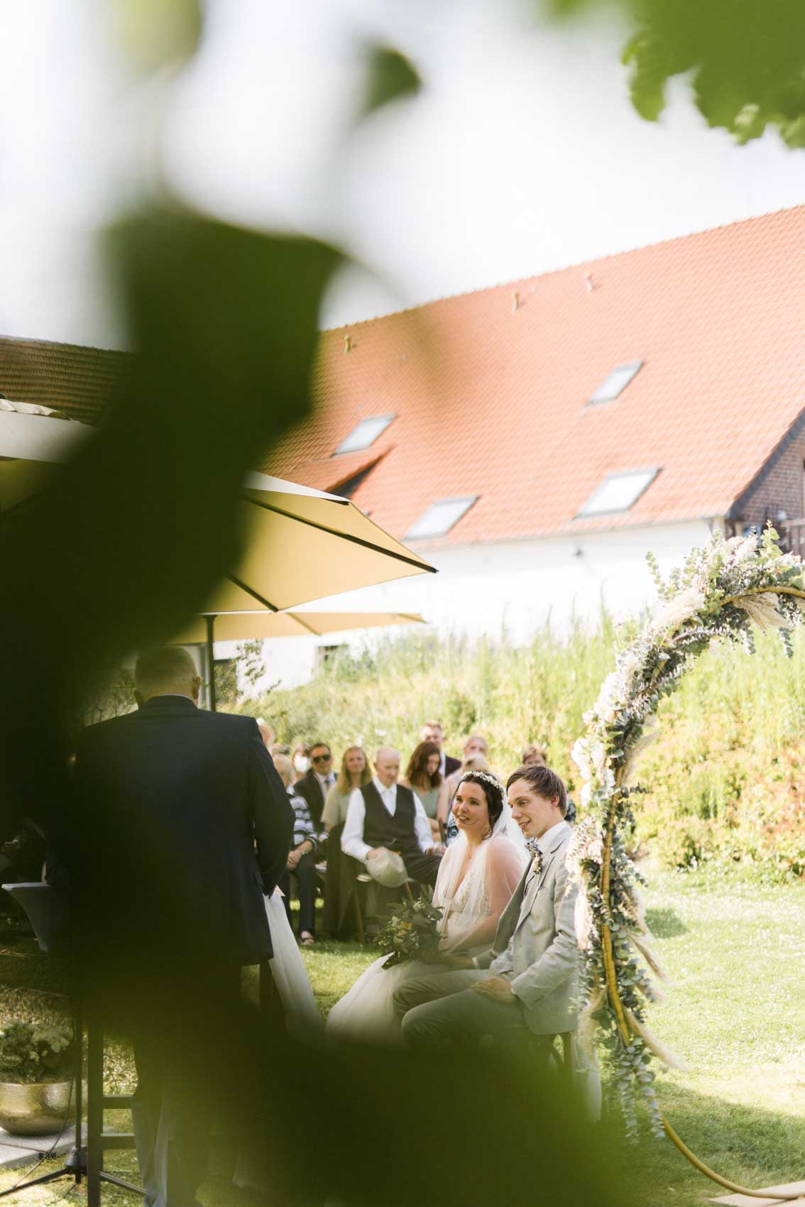 Brautpaar lauscht dem Trauredner bei einer freien Trauung im Garten der Hochzeitslocation Seescheune am Bulderner See in Dülmen