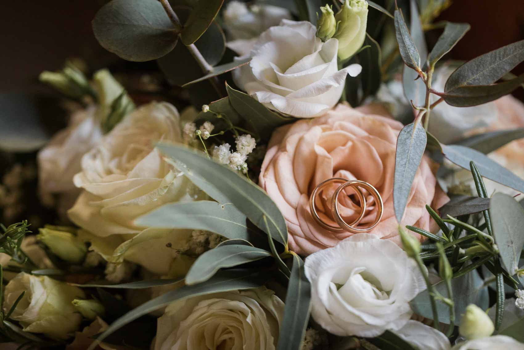 Trauringe auf einer pfirsichfarbenen Rose im Brautstrauß