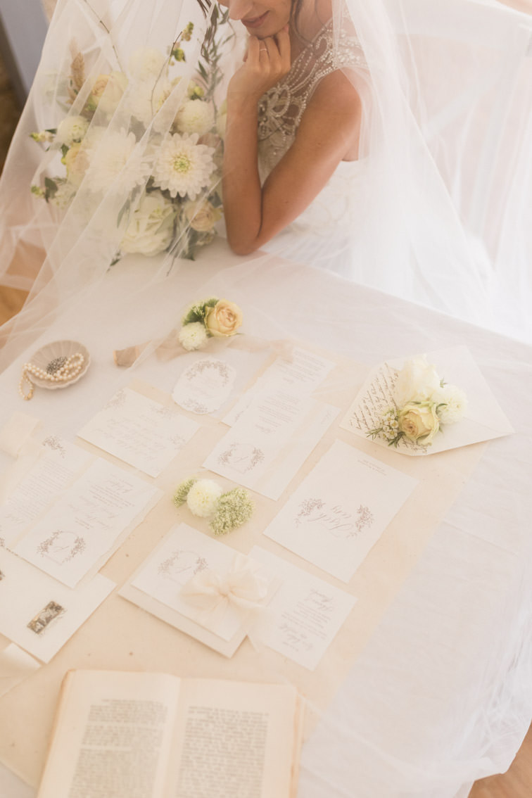 Braut mit Schleier schaut von oben auf Hochzeitspapeterieset designt von Jubelzeiten für ein Hochzeitsinspirationsshooting auf Haus Marck in Tecklenburg
