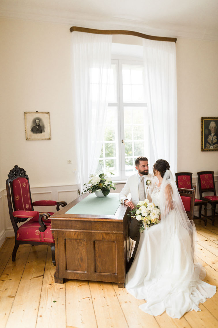 Braut mit langem Schleier sitzt mit ihrem Bräutigam am Trautisch im Landratszimmer vor einer standesamtlichen Trauung auf Haus Marck in Tecklenburg