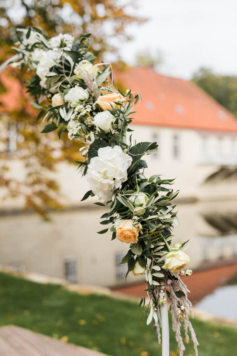Mit weißen Dahlien, Hortensien und cremefarbenen Rosen geschmückter Traubogen bei einer freien Trauung auf Haus Marck in Tecklenburg.