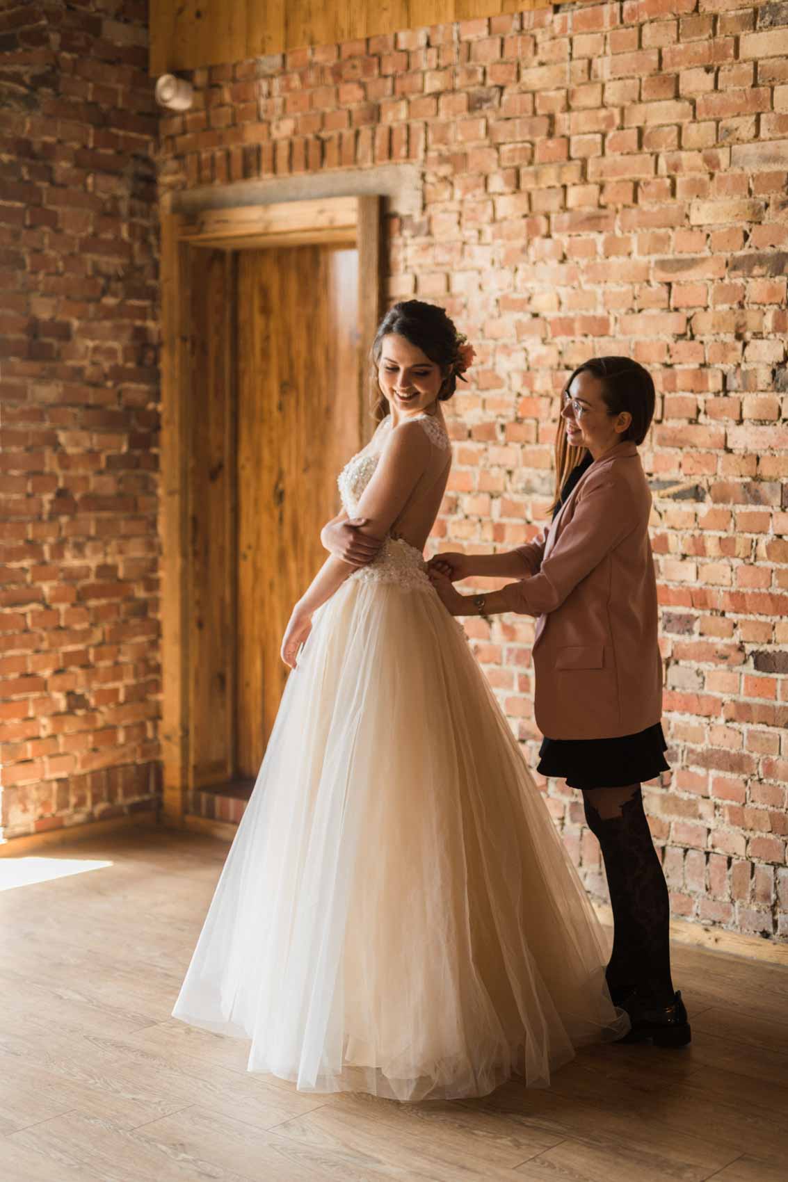 Hochzeitsplanerin Jana Opitz hilft Braut beim Anziehen des Brautkleids bei einem Styled Shoot auf Hof Frien